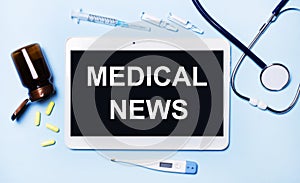 Ampoules, pills, stethoscope, thermometer, tablet with MEDICAL NEWS text on desktop.