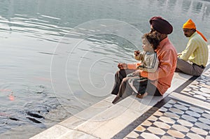 Amritsar, India - November 21, 2011: A Sikh family of pilgrims, father and son, are sitting near a lake in the Golden Temple