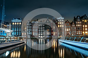 Amsterdam canal Singel with dancing houses and houseboats at night with reflection of illumination in water, Netherlands