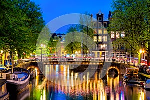 Amsterdam canal with typical dutch houses and bridge during twilight blue hour in Holland, Netherlands.