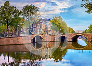Amsterdam Downtown. Beautiful sky at sunrise, old houses, canals and bridges. Calm reflections in the water. Heart of Amsterdam