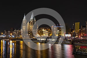 Amsterdam/Holland - October 06 2019: Night city view of Amsterdam canal, Basilica of Saint Nicholas and Barbizon Palace,