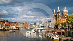 Amsterdam, Netherlands. View of Central Train Station, canal with boats, Basilica of Saint Nicholas in the old town.
