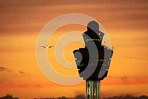 Amsterdam Schiphol International Airport control tower with a plane landing in the background during sunset