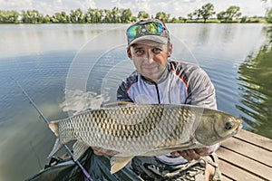 Amur fishing. Fisherman with grass carp fish in hands at lake