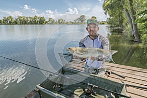 Amur fishing. Fisherman with grass carp fish in hands at lake