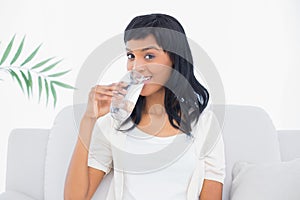 Amused black haired woman in white clothes enjoying a glass of water