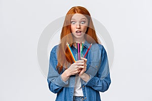 Amused and excited, wondered cute teenage redhead, foxy girl in denim shirt, stare at colored pencils fascinated, got