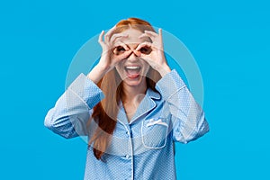 Amused girl seeing wonderful promo, want try out. Attractive redhead woman in lovely pyjama make glasses with fingers