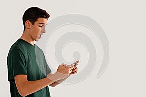 Amused handsome teenager playing games on smartphone. A lot of copy space