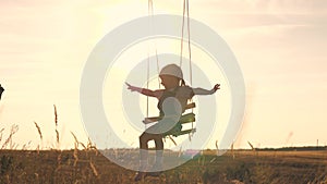 Amusement park dream concept. Happy girl swinging on a swing in the park at sunset. child plays with wooden swing