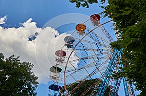 Amusement park ferris wheel, blue sky with clouds, green trees