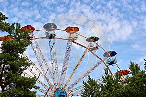 Amusement park ferris wheel, blue sky with clouds, green trees