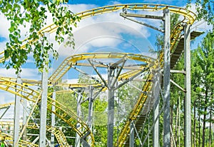 Amusement Park roller coaster ride, against the background of trees and blue sky in bright sunlight, no one