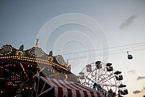 Amusement park with a vintage carousel with lights and a ferris wheel with colorful booths in the evening. Amusement park