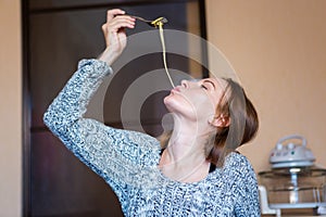 Amusing attractive young woman eating pasta in kitchen