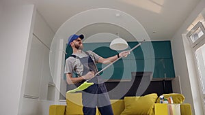 Amusing bearded man from cleaning service playing rock music using a mop as a guitar