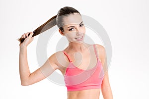 Amusing cheerful fitness girl holding her long hair in ponytail