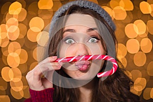 Amusing cute curly girl making funny face using candy cane