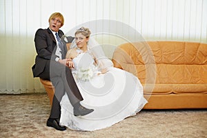Amusing groom and bride sitting on armchair