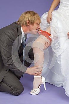 Amusing groom removes a garter from leg of bride photo