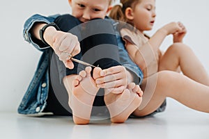 Amusing kids with bare feet leaning on each other, boy is clipping nails