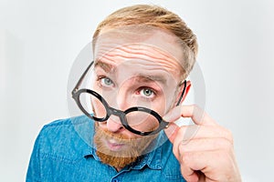 Amusing young man with beard looking over black round glasses