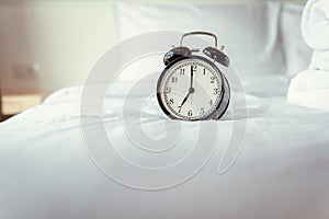 Analog Alarm Clock on Bedroom in Modern House, Retro Timer at 7.00 a.m. on White Cover Bed