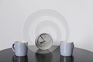 Analog alarm clock and cups on table
