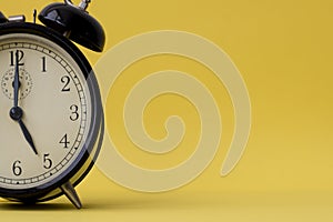 Analog alarm clock displaying five o`clock on a yellow background with copy space