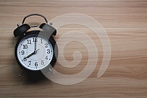 Analog alarm clock is placed on wooden table.