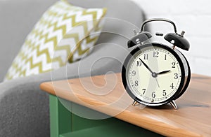 Analog alarm clock on side table in living room, space for text.