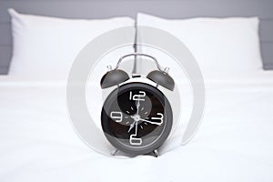 Analog alarm clock is on white bed, Time in the morning