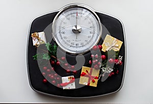 Analog scale surrounded by Christmas decorations. Overweight left after Christmas holidays.