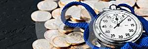 Analog stopwatch and pile of gold coins on a black background close-up. Counting time by stopwatch. Time measurement