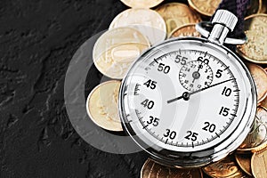 Analog stopwatch and pile of gold coins on a black background close-up. Counting time by stopwatch. Time measurement