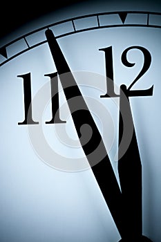 Analog wall clock in a low light with black hands and numbers with few minutes left to 12 hour