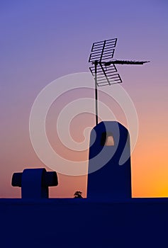 Analogue antenna silhouette on roof at sunset