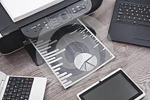 Analyzing investment charts with printer and laptop