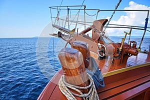 A anchor, ropes and bow of a wooden sailing yacht against the background of the sea and the blue sky