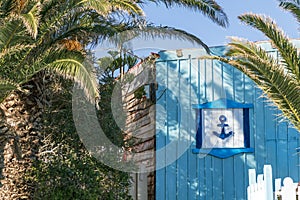 Anchor symbol of summer sea tourism and holidays on the beautiful wooden blue fence with entrance door in the shadow of palm tree