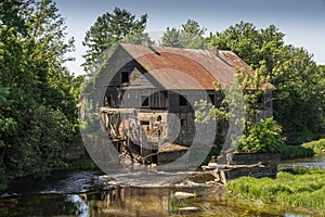 Ancient abandoned water mill surrounded by beautiful nature. House built of stone and wood, exterior walls and dilapidated bridge