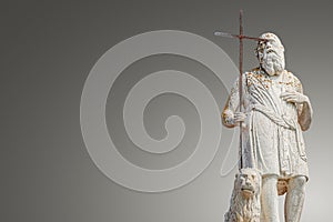 Ancient aged sculpture of poor bearded stranger pilgrim in lichen with cross and pet lion at roof of Santa Maria Assunta Jesuits photo