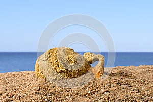 Ancient amphora lying on the sand against the blue sky, found in Greece