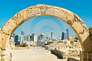 Ancient arch at Bahrain Fort with skyline of Manama. A UNESCO World Heritage Site