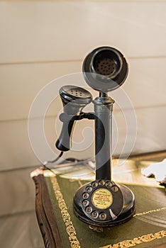 Ancient black candlestick telephone vintage analog dialing or scrolling phone on wooden table interior for home and living