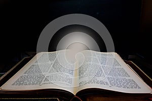 Ancient book which leads to a source of light against a black background