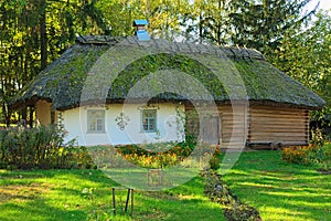 Ancient clay house with thatched roof and front yard with flower bed
