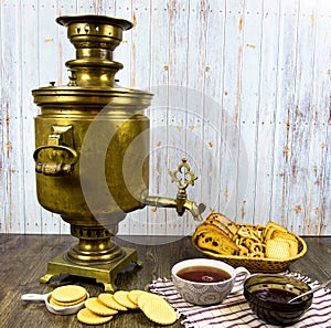 Ancient copper samovar on a wooden table with a Cup of tea breadcrumbs biscuits jam.