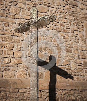 Ancient cross on stone wall. Stone old crucifix with shadow on monastery backyard. Christianity symbols. Medieval cemetery.